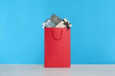 Photo of Paper shopping bag full of gift boxes on light blue background