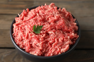 Raw ground meat and parsley in bowl on wooden table, closeup