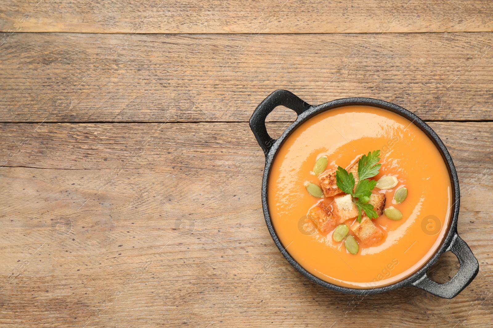 Photo of Tasty creamy pumpkin soup with croutons, seeds and parsley in bowl on wooden table, top view. Space for text