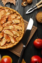 Photo of Delicious apple pie and ingredients on black wooden table, flat lay