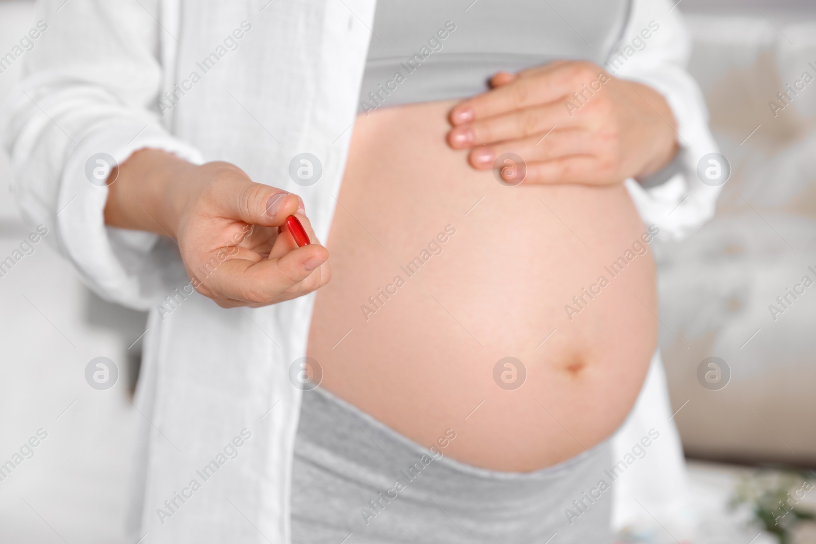 Photo of Pregnant woman holding red pill indoors, closeup