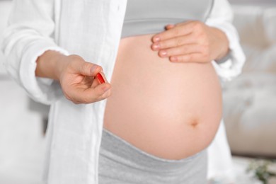 Pregnant woman holding red pill indoors, closeup