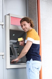 Young man using cash machine for money withdrawal outdoors