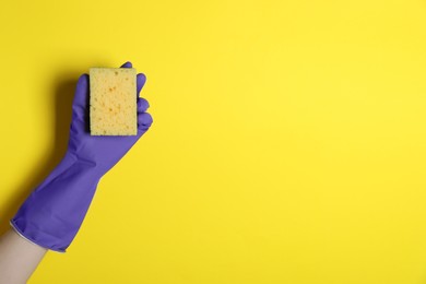 Woman in rubber glove holding sponge on yellow background, top view. Space for text
