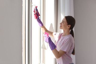 Photo of Young woman cleaning window glass with rag and detergent at home