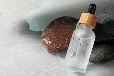 Photo of Bottle of face serum and spa stones on wet grey marble table, closeup. Space for text