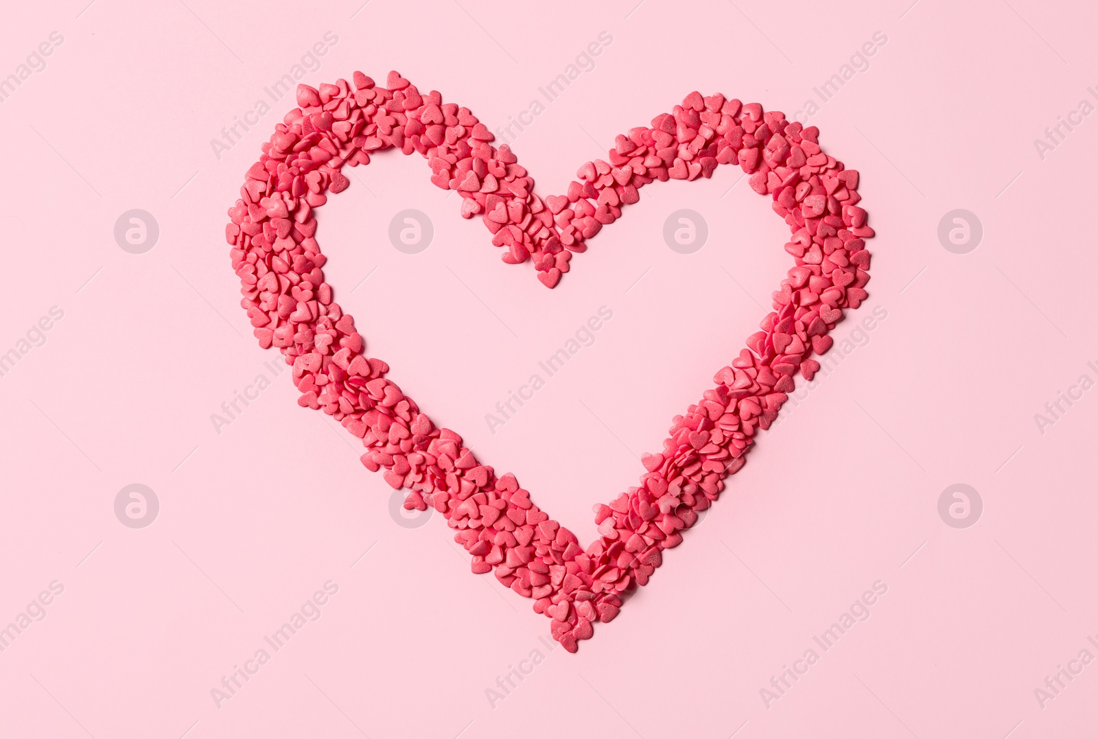 Photo of Heart made with sprinkles on pink background, top view