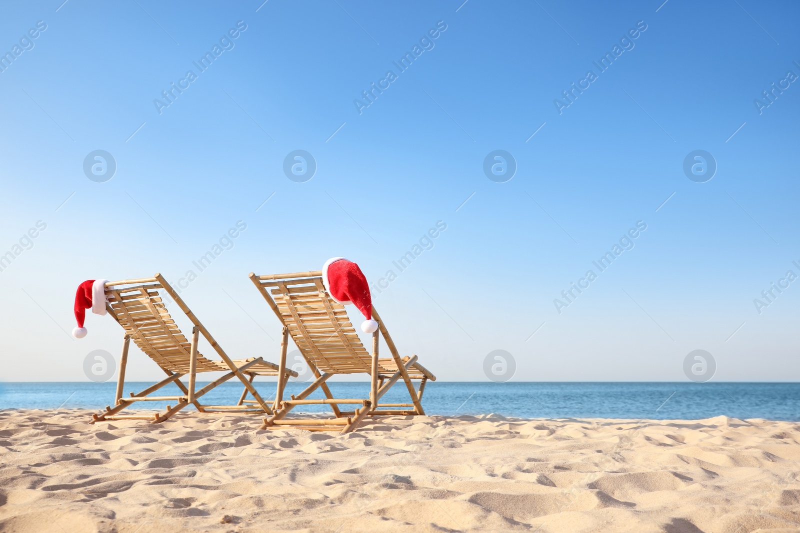 Photo of Sun loungers with Santa's hats on beach, space for text. Christmas vacation