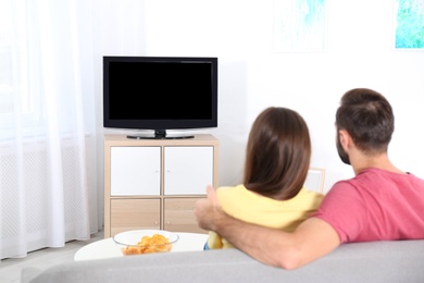 Photo of Young couple watching TV on sofa at home