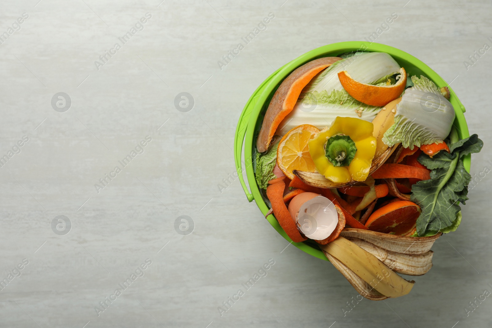 Photo of Natural garbage in trash bin on light background, top view with space for text. Composting of organic waste