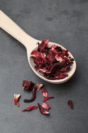 Hibiscus tea. Wooden spoon with dried roselle calyces on grey table, closeup
