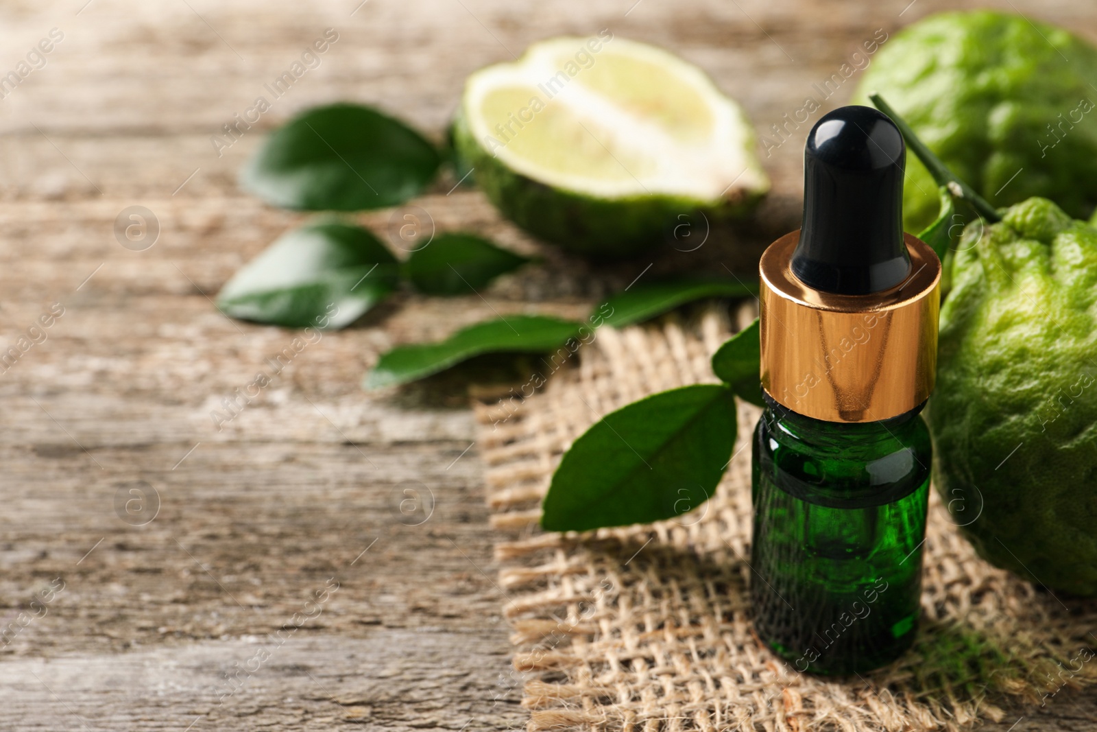 Photo of Bottle of essential oil and fresh bergamot fruits on wooden table, closeup. Space for text