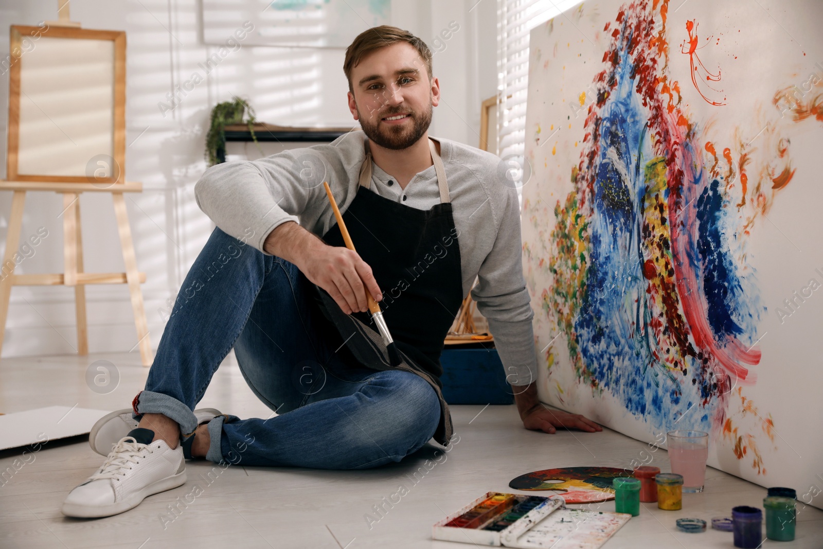 Photo of Young man with painting brush near canvas in artist studio