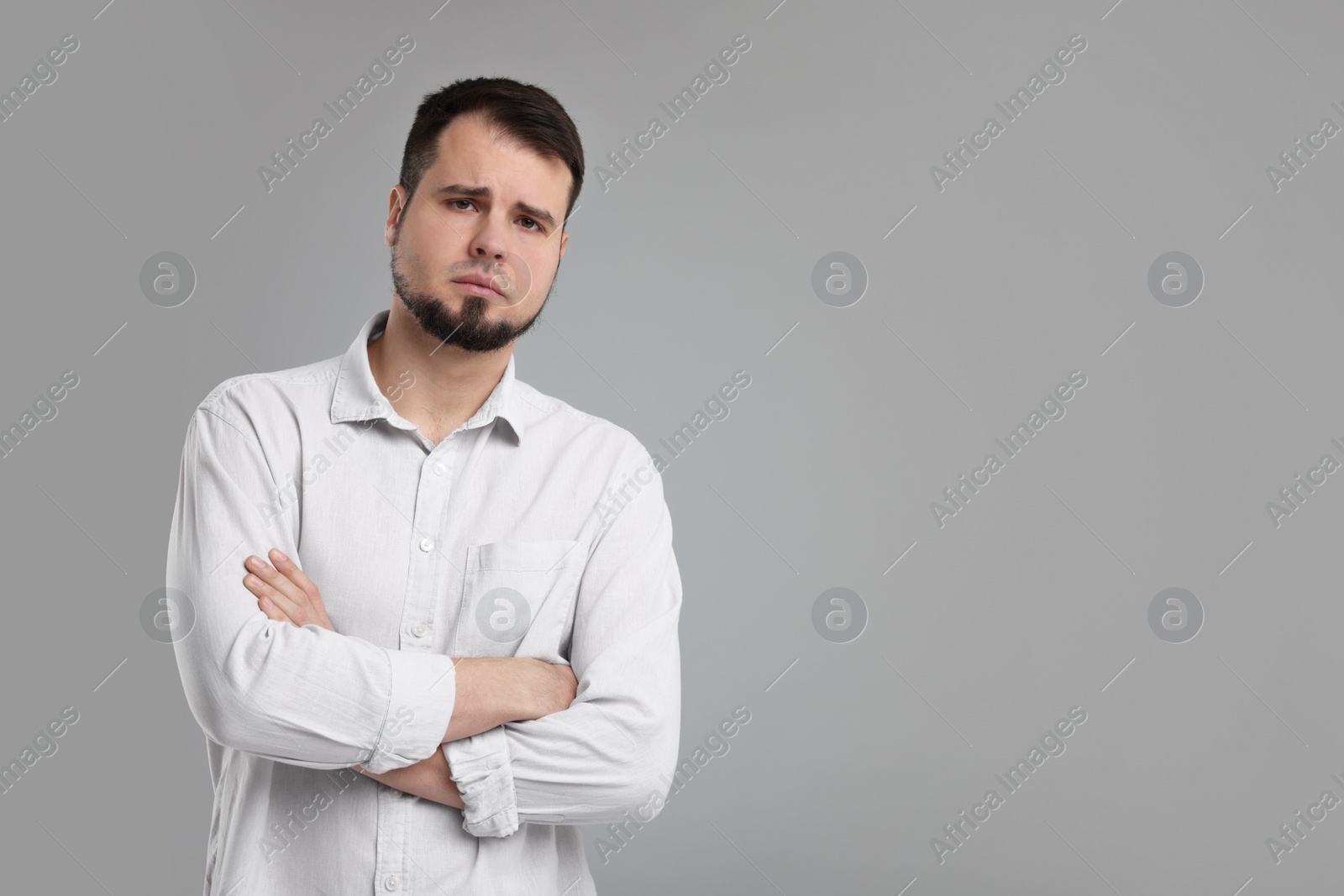 Photo of Portrait of sad man with crossed arms on grey background, space for text