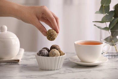 Photo of Woman taking delicious vegan candy ball at white marble table indoors, closeup