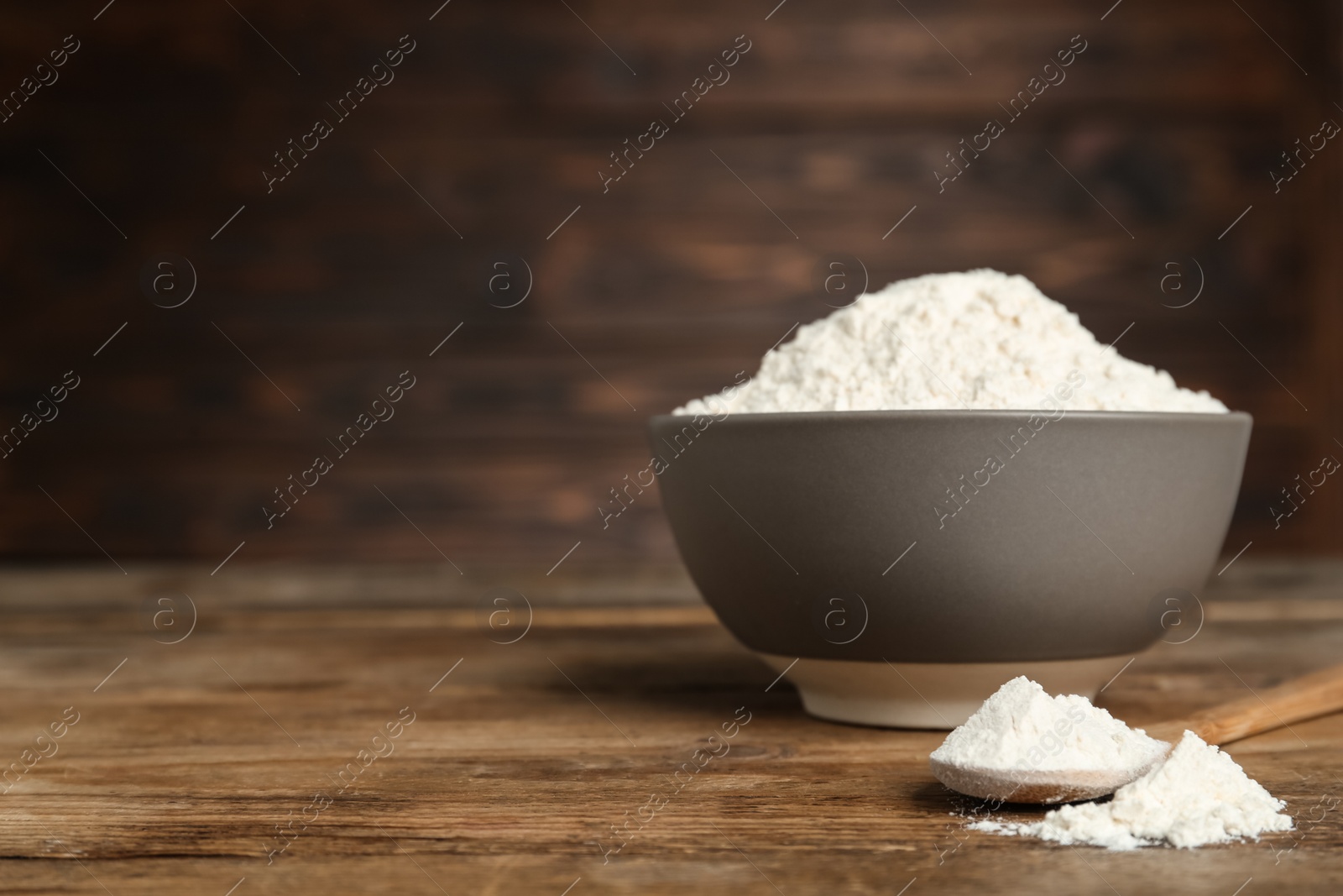Photo of Ceramic bowl and spoon with flour on wooden table, space for text. Cooking utensil