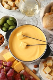 Photo of Pot of tasty cheese fondue, snacks and wine on white marble table, flat lay