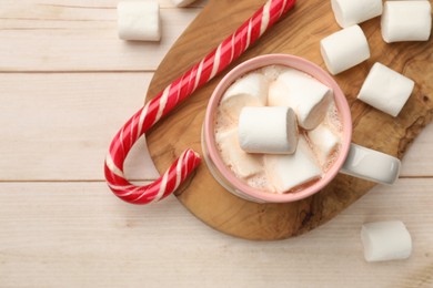 Photo of Tasty hot chocolate with marshmallows and candy cane on light wooden table, top view