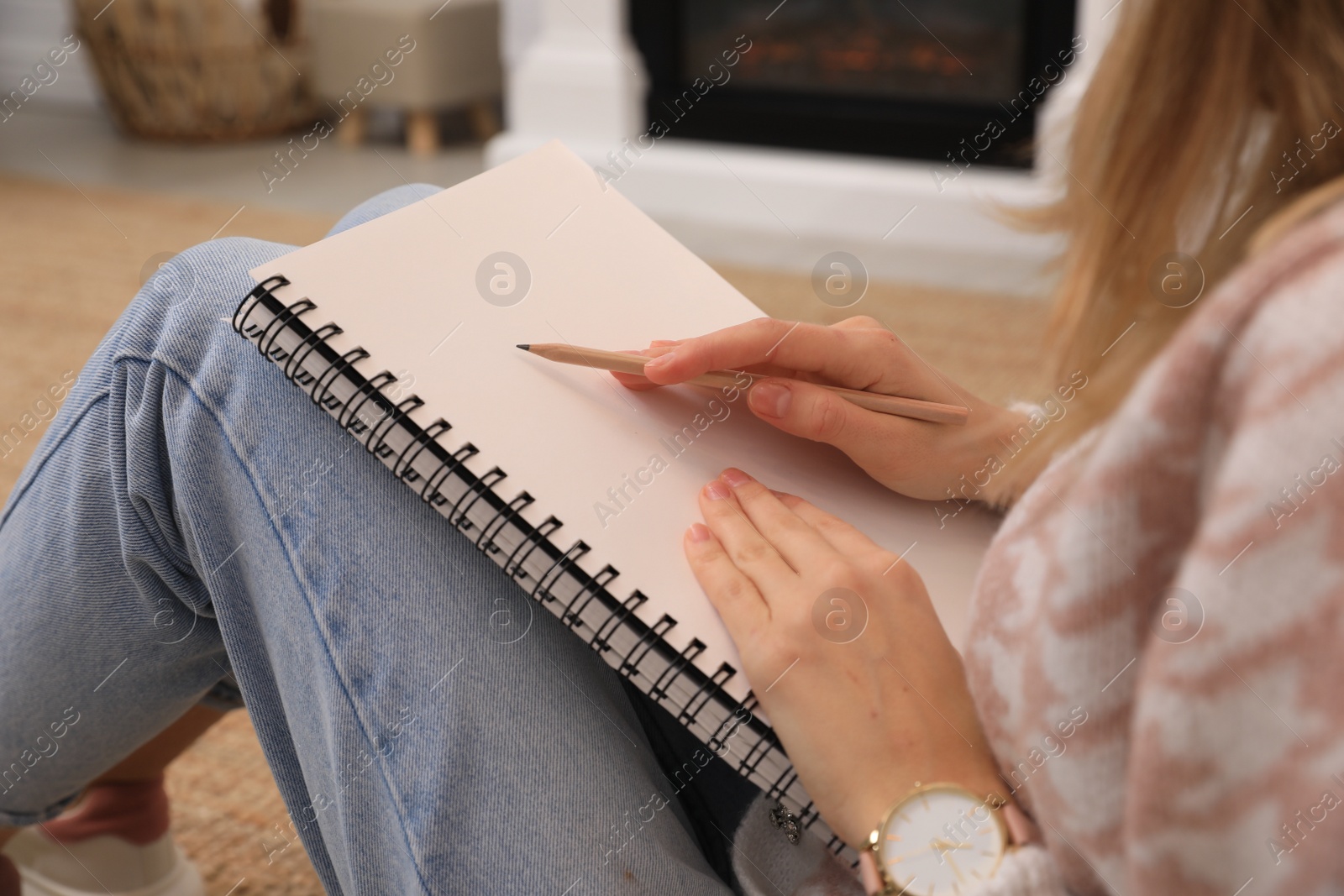 Photo of Woman drawing in sketchbook with pencil on floor at home, closeup