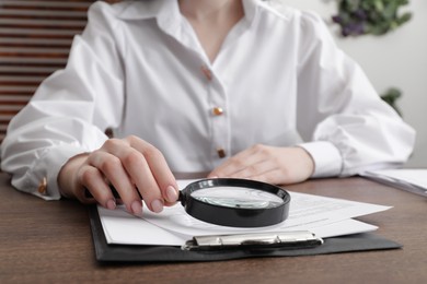 Photo of Woman looking at document through magnifier at wooden table indoors, closeup. Searching concept