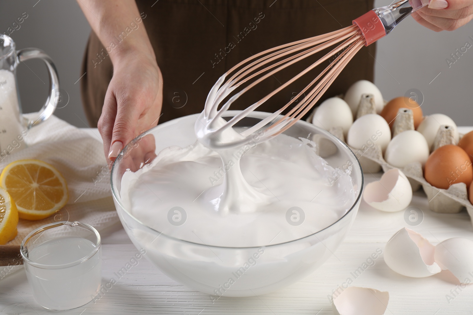 Photo of Woman making whipped cream with whisk at white wooden table, closeup