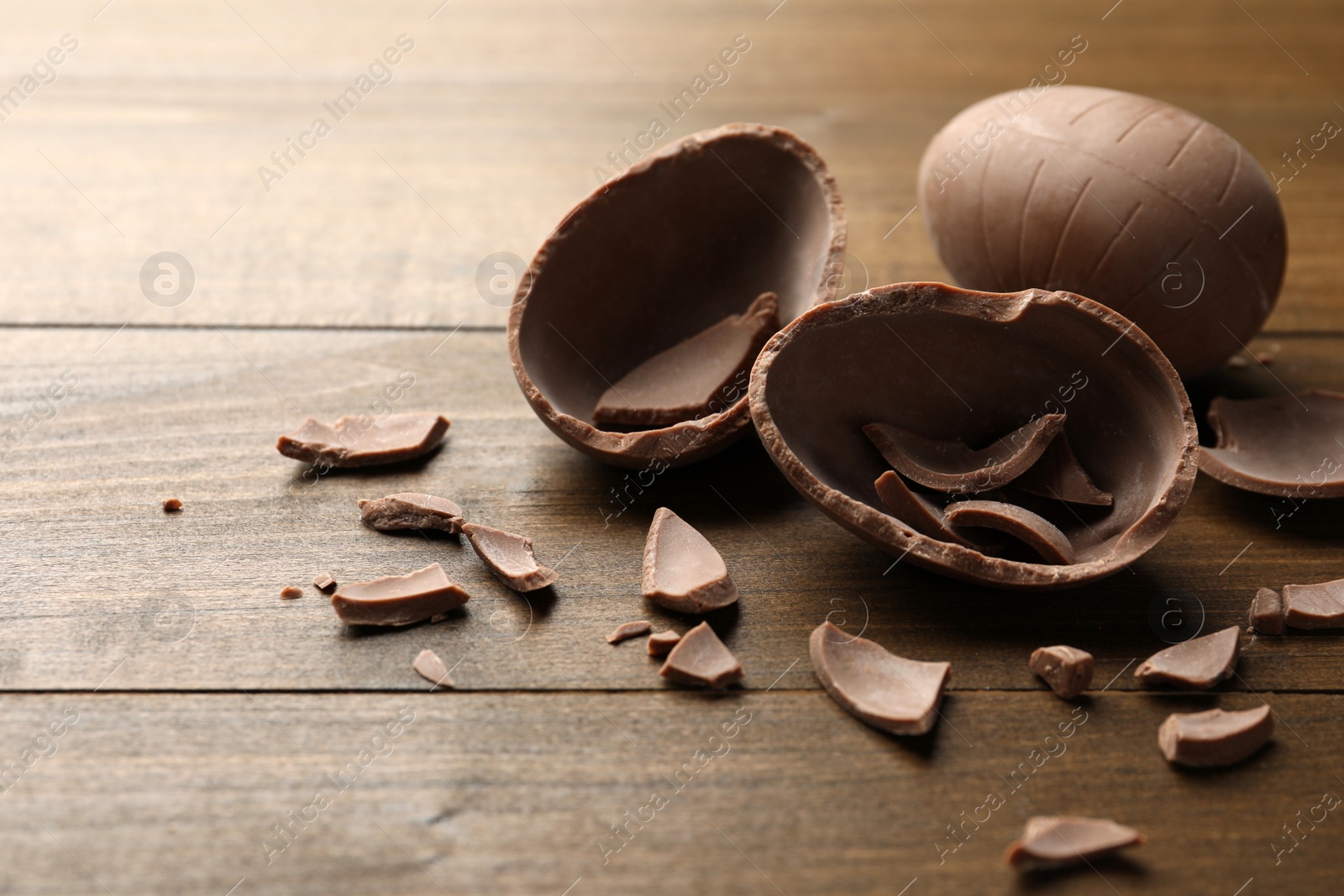 Photo of Broken and whole chocolate egg on wooden table, space for text