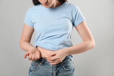 Diabetes. Woman making insulin injection into her belly on grey background, closeup