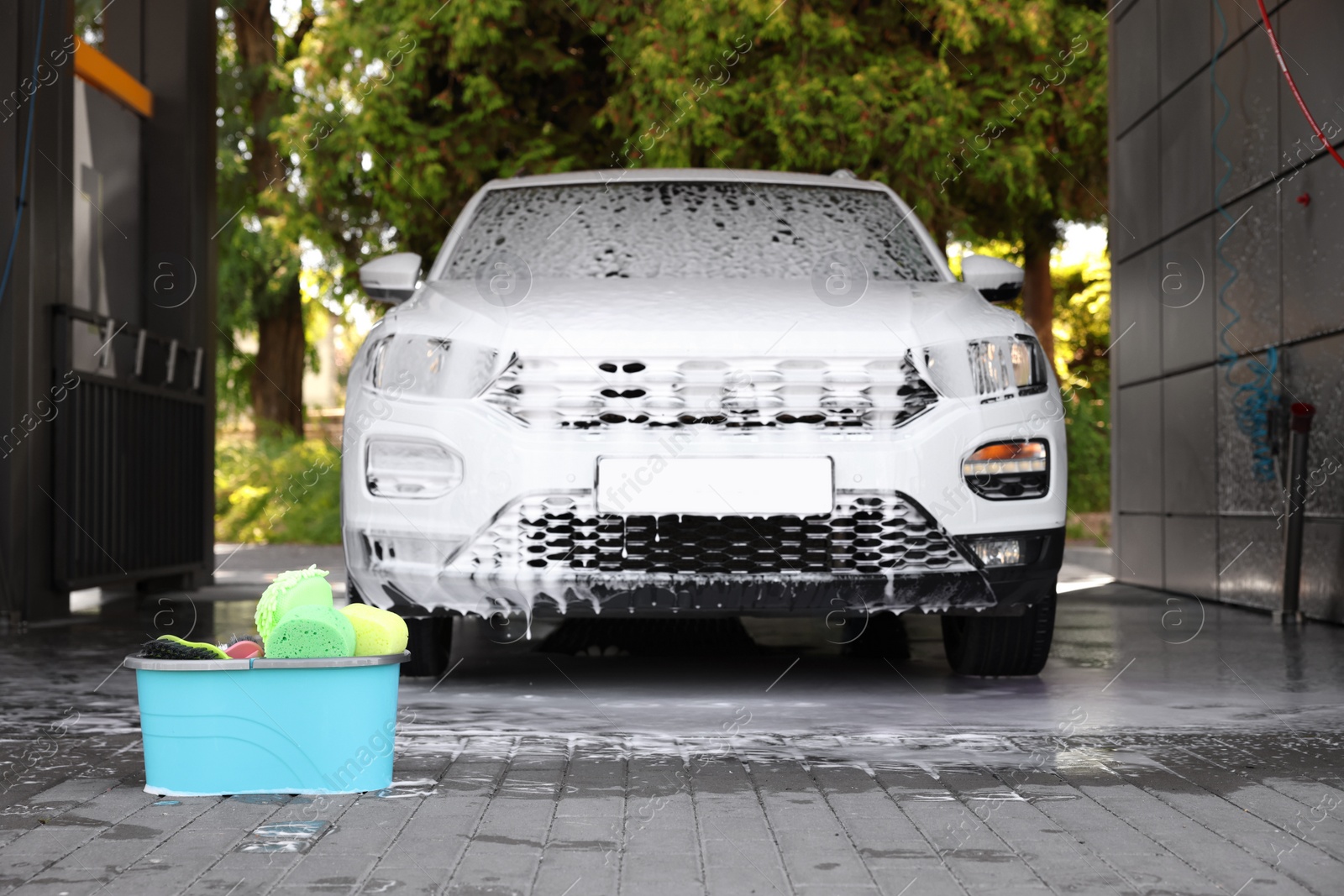 Photo of Auto covered with foam and cleaning products in bucket at outdoor car wash