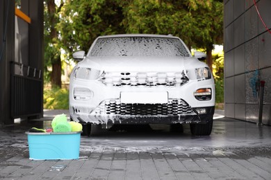 Photo of Auto covered with foam and cleaning products in bucket at outdoor car wash