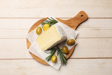 Photo of Board with piece of tasty camembert cheese, olives and rosemary on light wooden table, top view