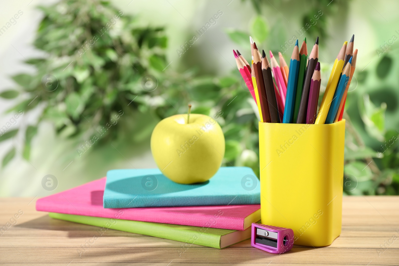 Photo of Different school stationery and fresh apple on wooden table against blurred background