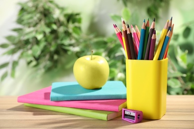 Photo of Different school stationery and fresh apple on wooden table against blurred background