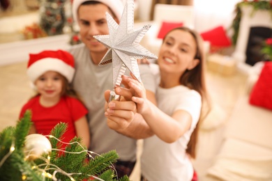 Family decorating Christmas tree indoors, focus on star topper