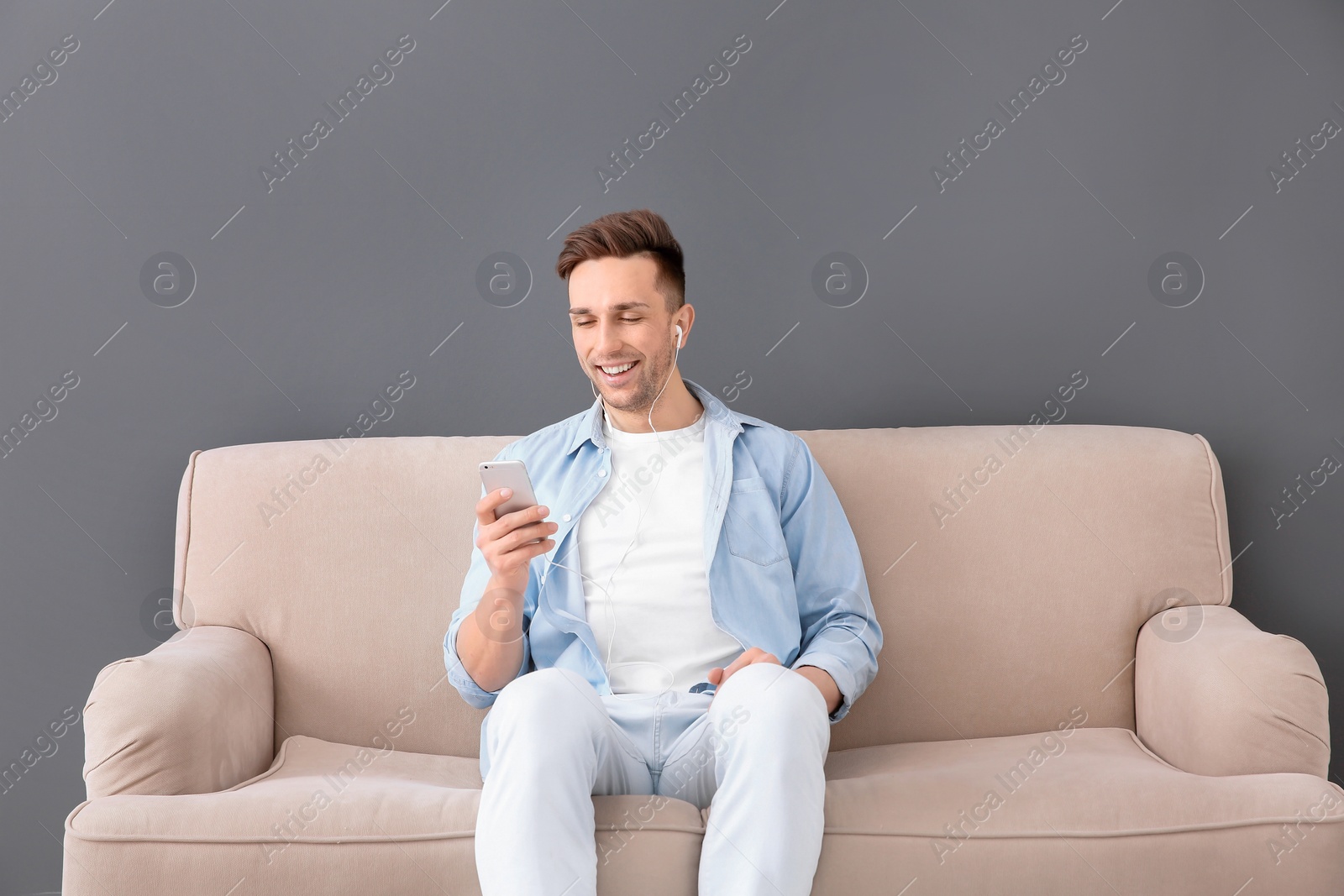 Photo of Handsome young man sitting on sofa and listening to music, indoors