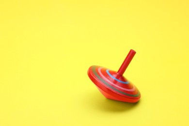 Photo of One bright spinning top on yellow background, space for text. Toy whirligig