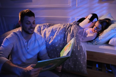 Photo of Father reading bedtime story to his daughter at home