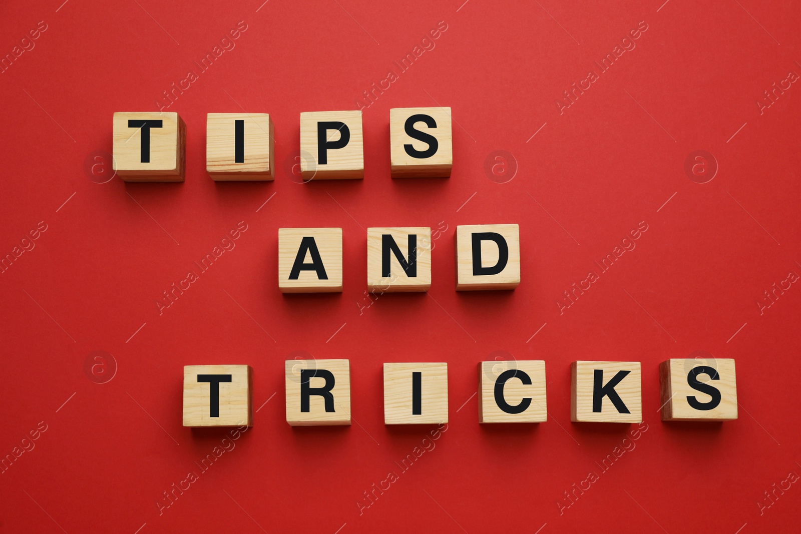 Photo of Phrase Tips And Tricks made of wooden cubes with letters on red background, flat lay