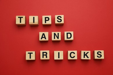 Photo of Phrase Tips And Tricks made of wooden cubes with letters on red background, flat lay