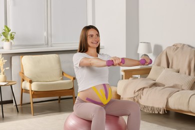 Beautiful pregnant woman with kinesio tapes doing exercises at home