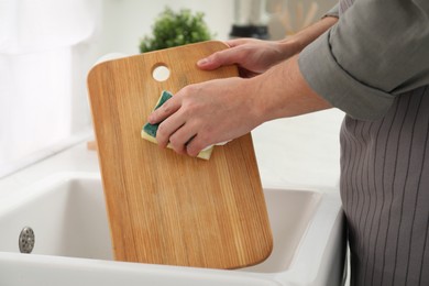 Photo of Man washing wooden cutting board at sink in kitchen, closeup