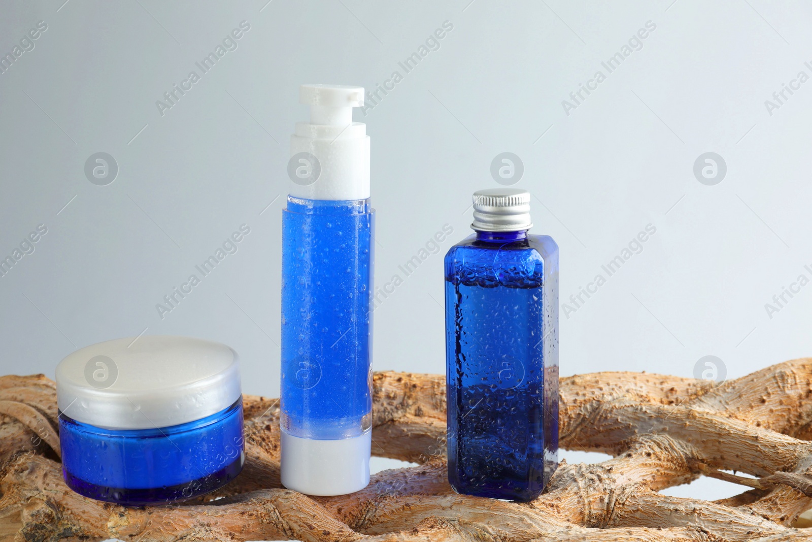 Photo of Set of cosmetic products on wooden branch against light grey background