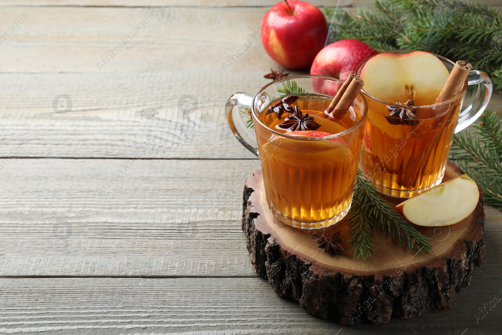 Photo of Hot mulled cider, ingredients and fir branches on wooden table, space for text