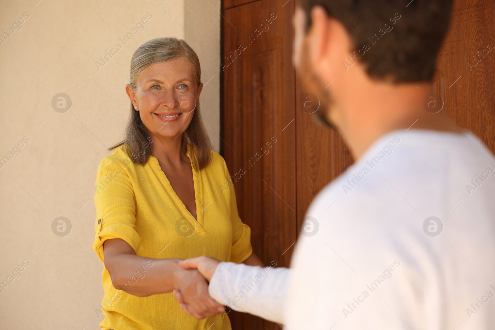 Photo of Friendly relationship with neighbours. Happy senior woman and man shaking hands near house outdoors