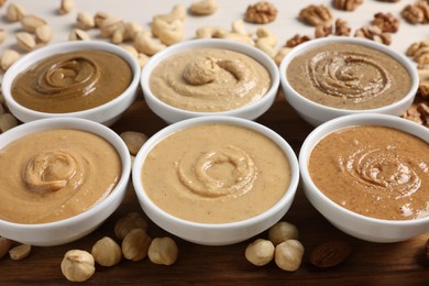 Photo of Many tasty nut butters in bowls and nuts on table, closeup