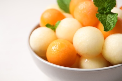 Photo of Melon balls and mint in bowl on white table, closeup