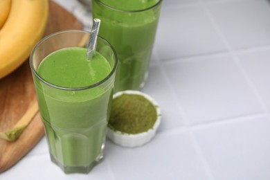 Glasses of tasty matcha smoothie on white tiled table, closeup. Space for text