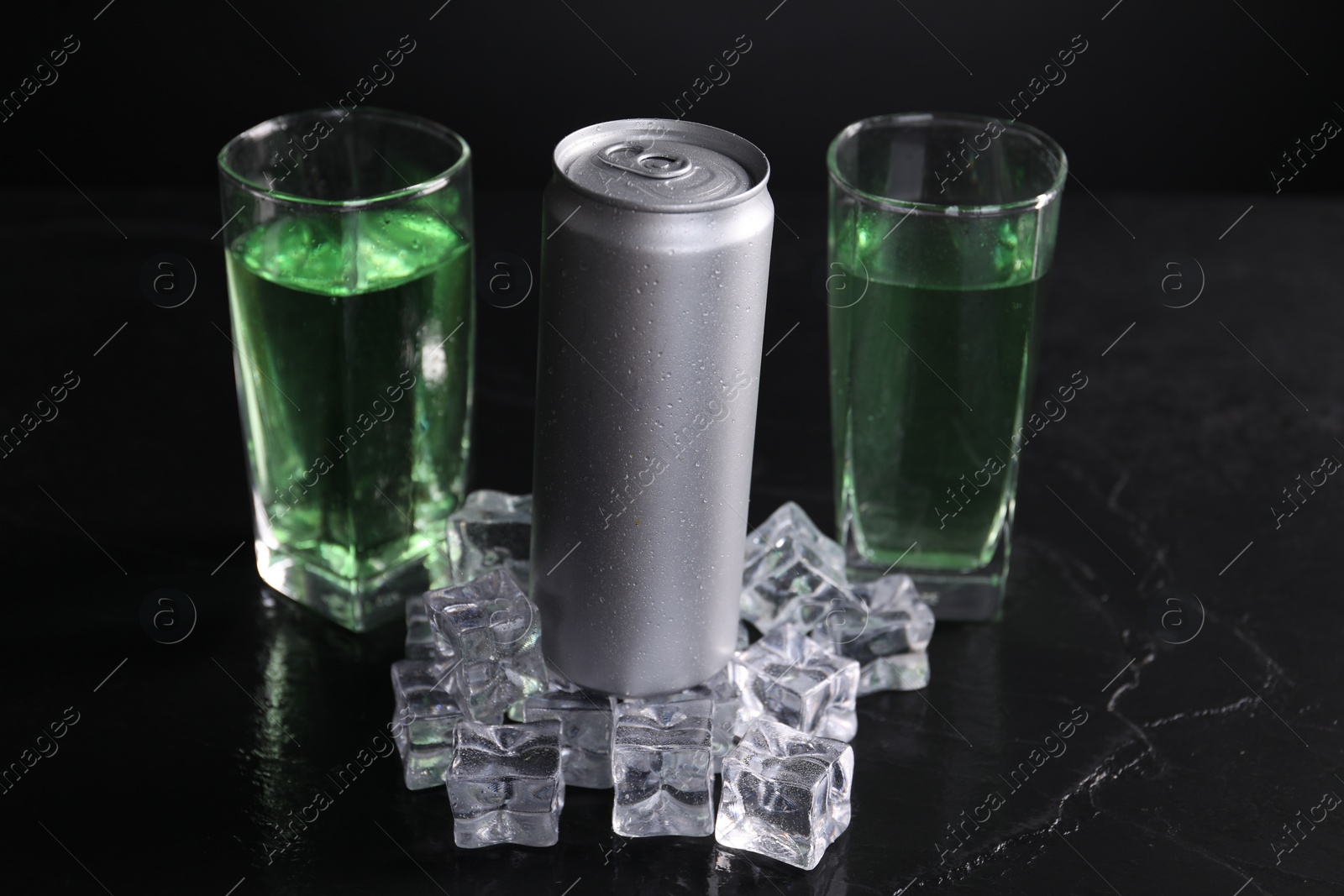 Photo of Energy drink in glasses, aluminium can and ice cubes on black table