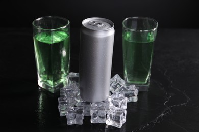 Energy drink in glasses, aluminium can and ice cubes on black table