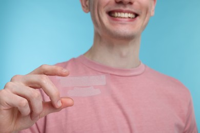 Photo of Young man with whitening strips on light blue background, closeup