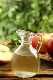 Photo of Natural apple vinegar on wooden table against blurred background